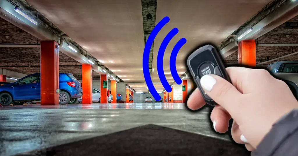 A person's hand holding a remote starter with bars going off it towards cars in a parking garage