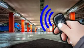 A person's hand holding a remote starter with bars going off it towards cars in a parking garage