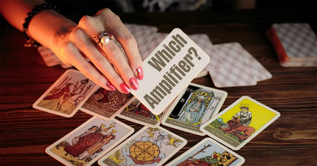 A woman's hand holding a sign saying 'which amplifier' and tarrot cards in the background on a table