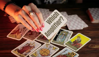 A woman's hand holding a sign saying 'which amplifier' and tarrot cards in the background on a table