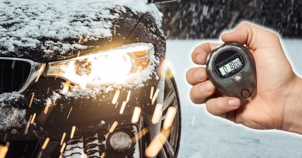 a black car in the snow with its headlight on and a hand holding a stopwatch off to the side