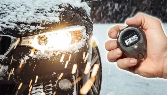 a black car in the snow with its headlight on and a hand holding a stopwatch off to the side